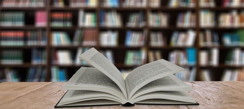 Libro abierto sobre mesa con biblioteca de fondo