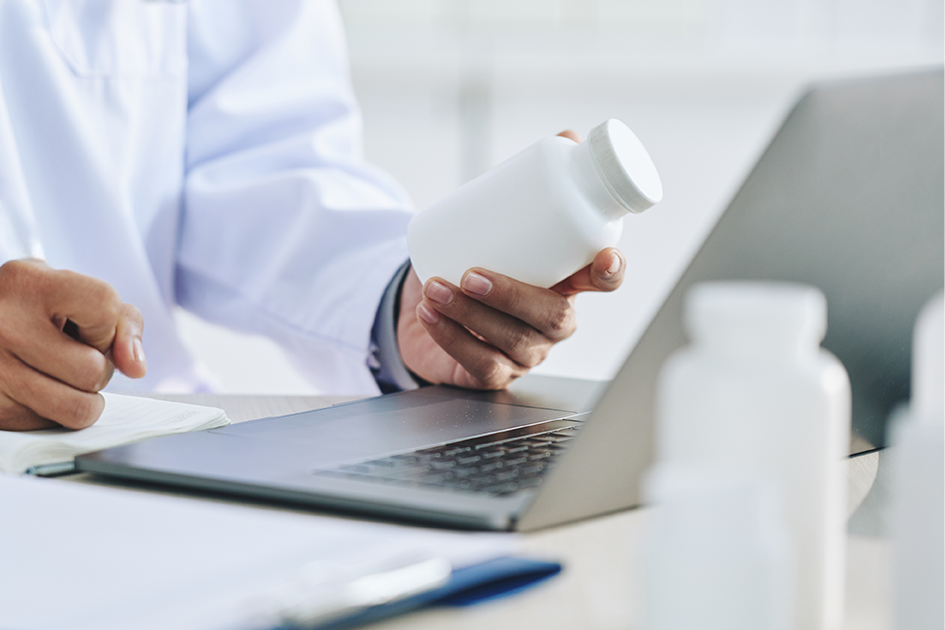 Profesional de la salud enfrente a una computadora y con un recipiente en la mano. Profesional de la salud enfrente a una computadora y con un recipiente en la mano.