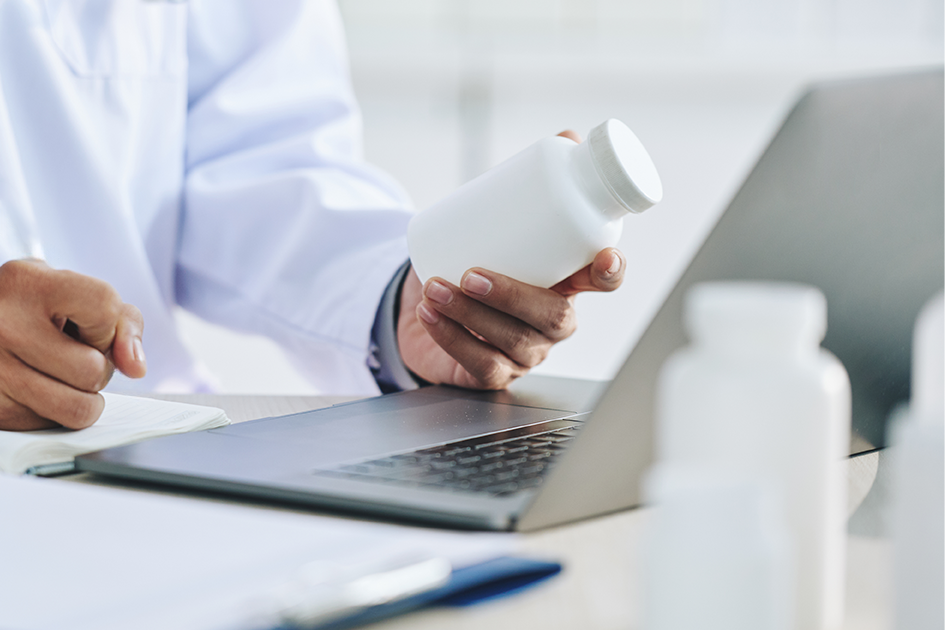 Profesional de la salud enfrente a una computadora y con un recipiente en la mano. 