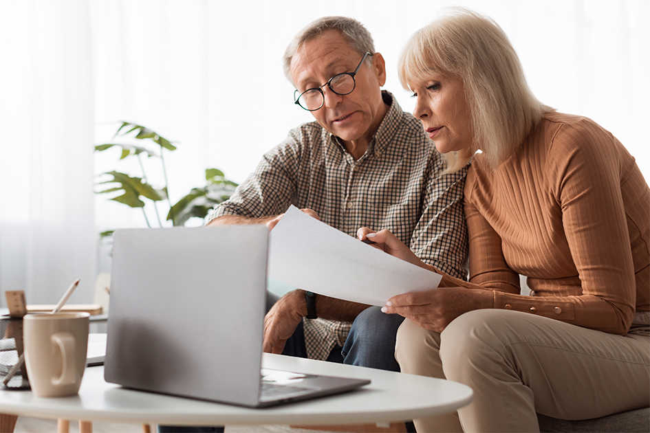 Dos adultos mayores mirando documentos y una computadora
