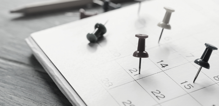 Hoja de calendario sobre mesa de madera con días señalados. 