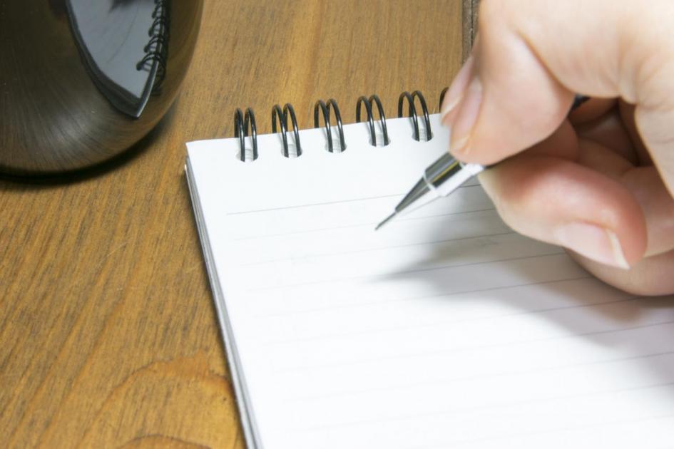 Nuevas funcionalidades Foto meramente descriptiva: una mano sostiene bolígrafo para escribir en una libreta.