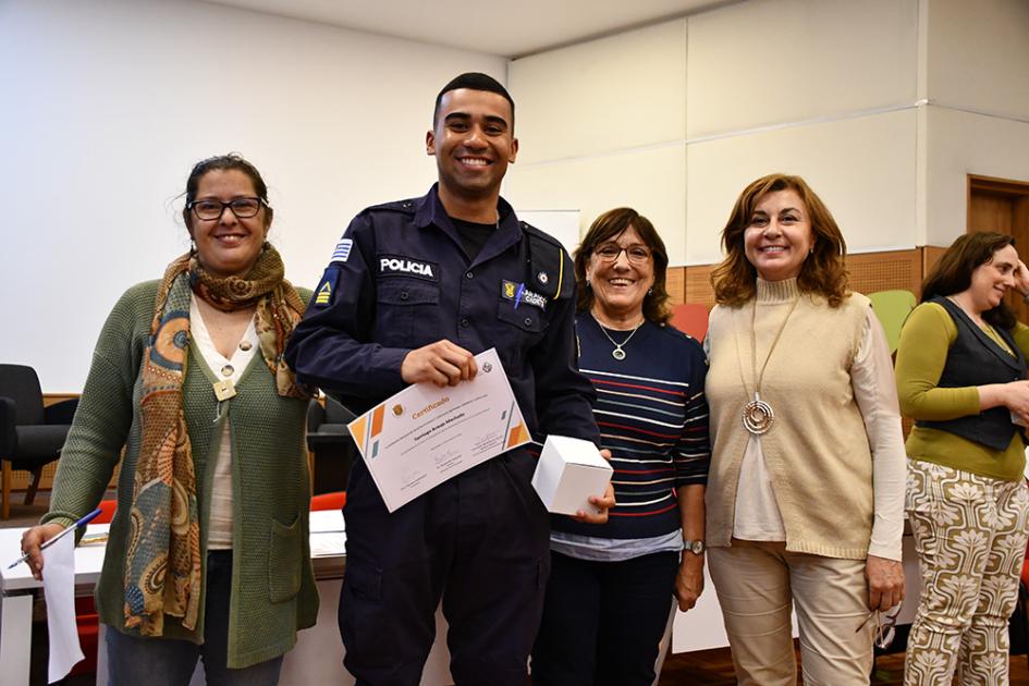 Entrega de diplomas a los participantes del curso docentes posan con uno de los participantes del curso, que viste el uniforme y muestra su diploma
