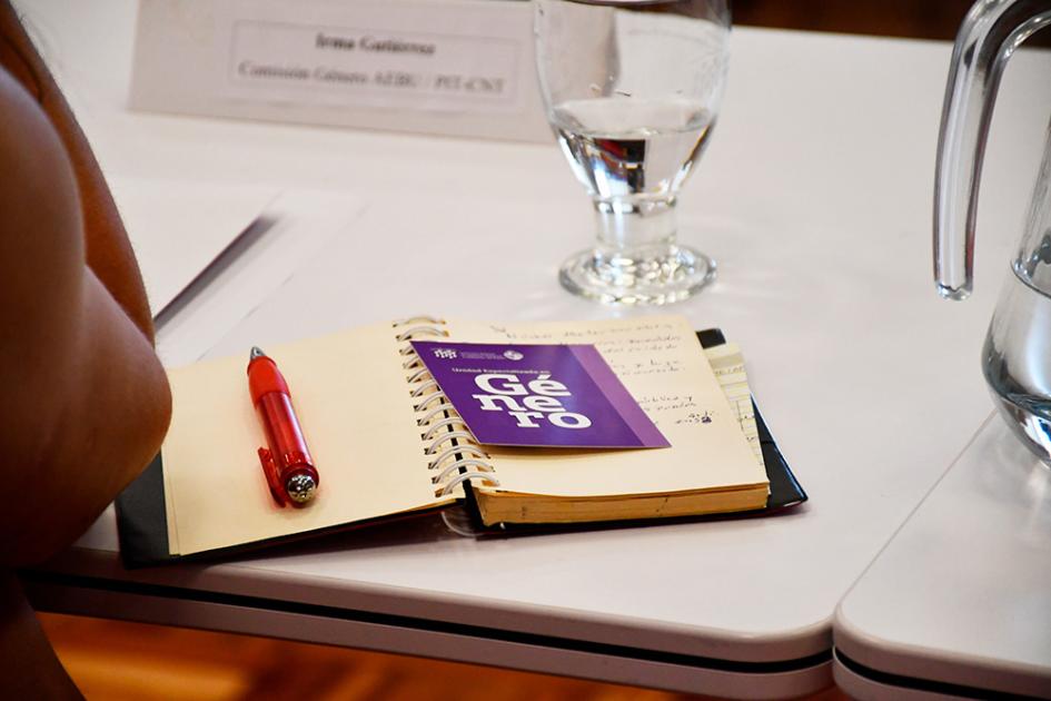 Mesa de diálogo sobre conciliación de la vida personal, familiar y laboral Postal sobre la Unidad Especializada en Género arriba del cuaderno de una participante