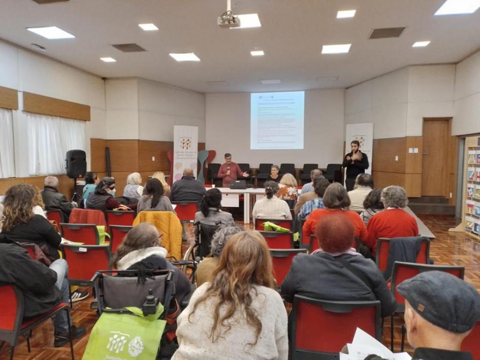 Asistentes atienden la presentación de la mesa de apertura Asistentes sentados atienden la presentación de la mesa de apertura que está frente a ellos