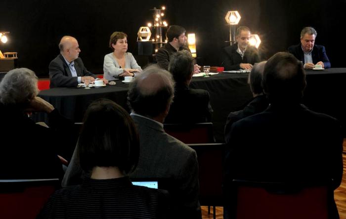 Se ve la mesa de panelistas, en un clima oscuro e íntimo, con presencia de público