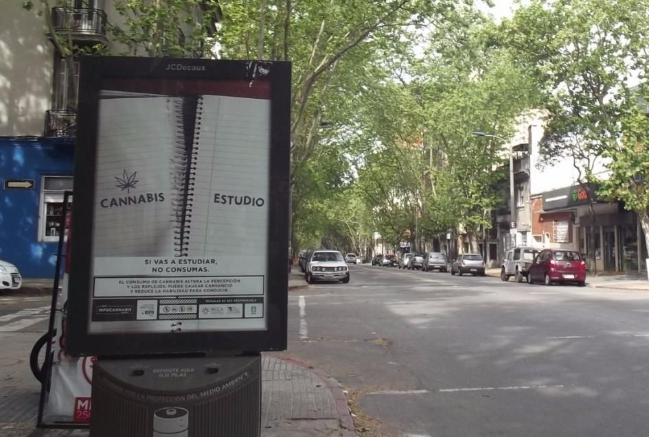 Afiche en vía pública con cuadernola de espiral con hoja arrancada que dice cannabis, con el mensaje si vas a estudiar no consumas