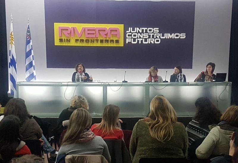 Público del evento visto desde atras. De frente mesa con cartel Rivera sin fronteras, Juntos construimos futuro. Exposición de Gabriela Olivera de la Secretaría Nacional de Drogas