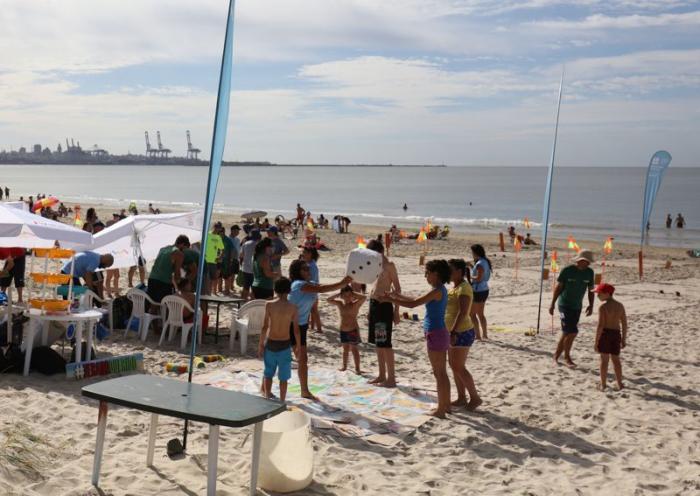 Público jugando con la rayuela interactiva en la playa. Sombrillas, flybanners y canchas de tejo