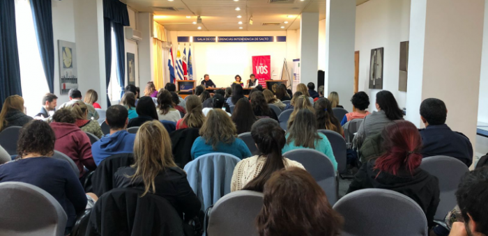 imagen del salón. Se ve el público desde atrás el público y en la mesa los ponentes Silva, Cirio y Martínez