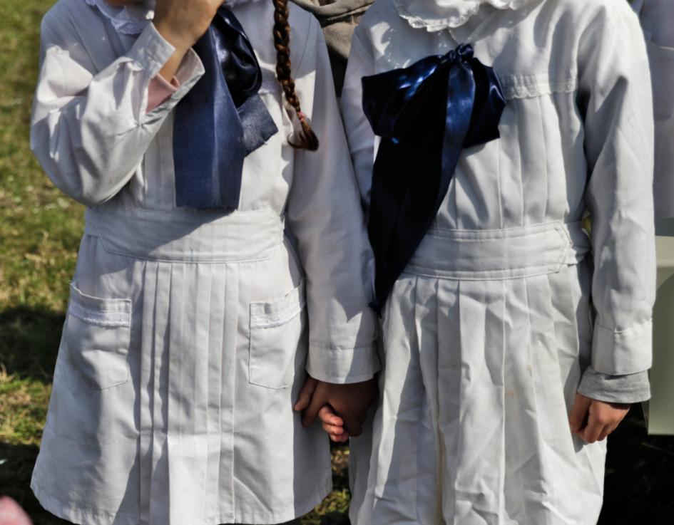 Dos niñas con las túnicas y los moños de la escuela pública se toman de la mano