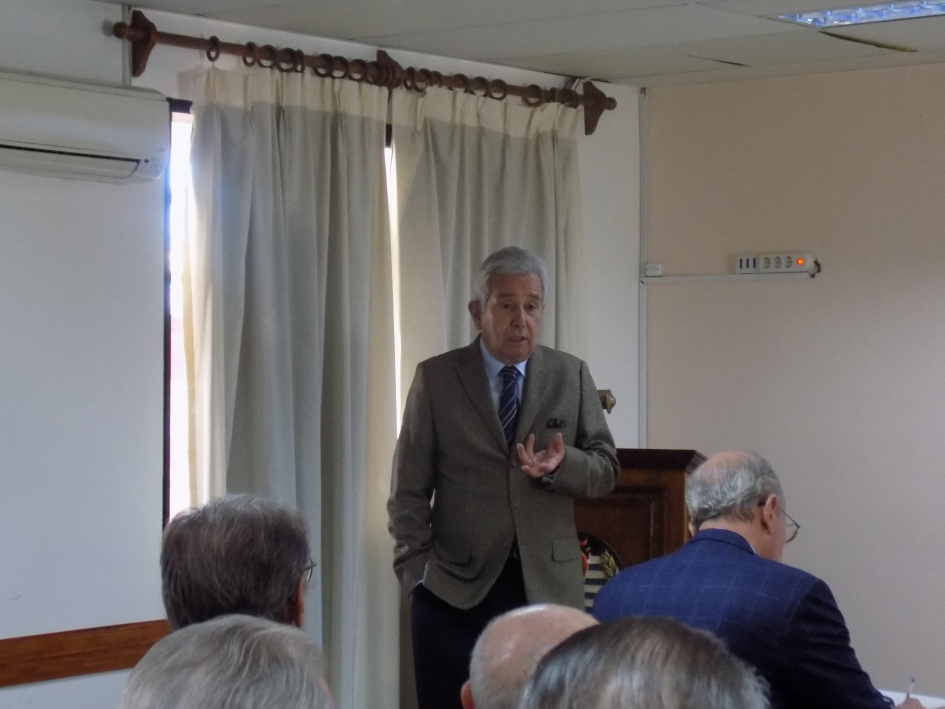 Presentación de tesis: expositor de pie junto a pantalla, público lo escucha sentado. Presentación de tesis: expositor de pie junto a pantalla, público lo escucha sentado.