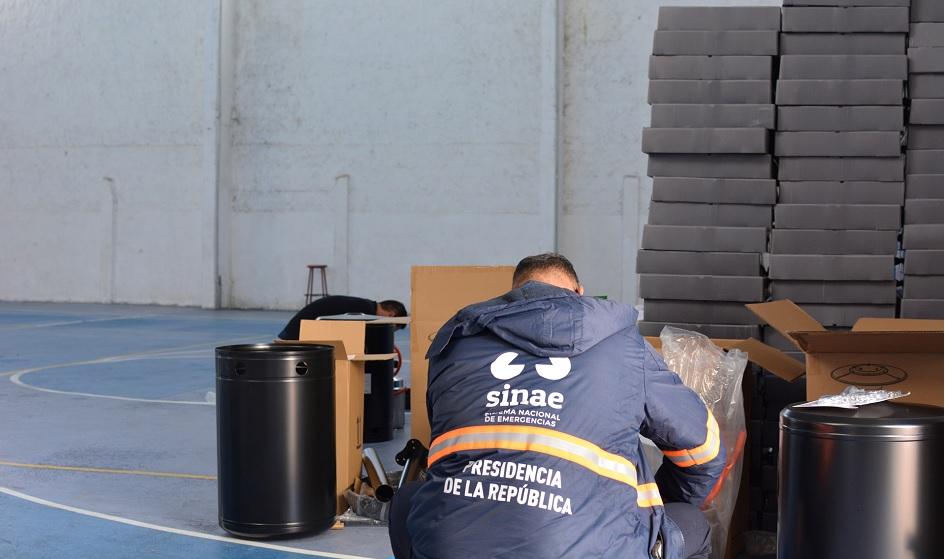 Persona agachada con campera de sinae trabajando en un centro de evacuados
