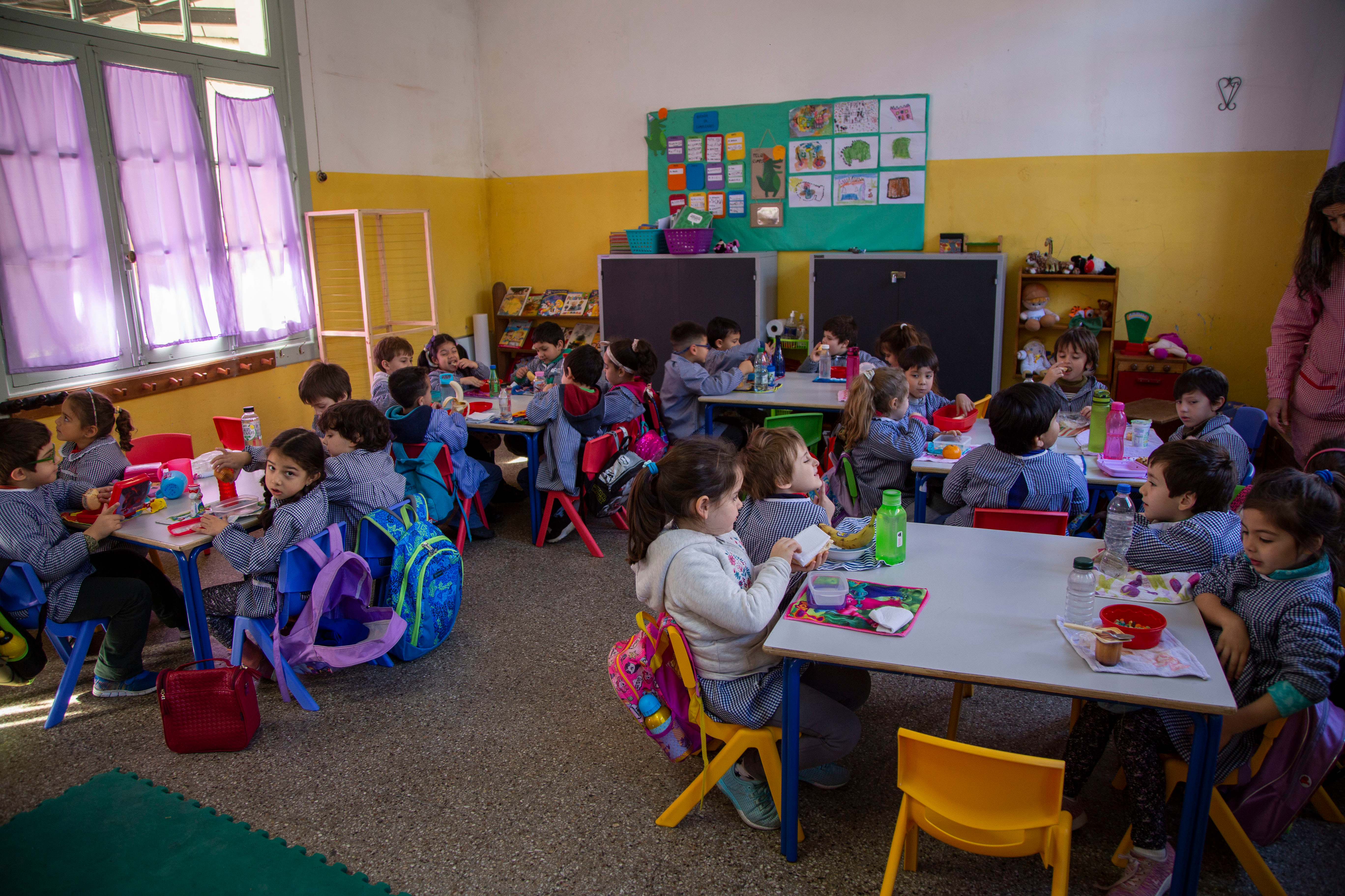 Aula de educación inicial en la que se ven aproximadamente 20 niños y una maestra