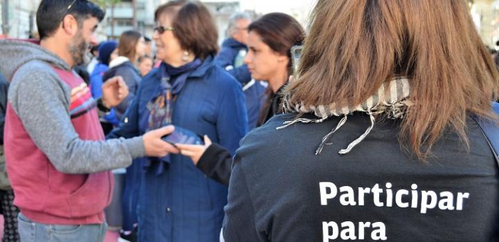 Participantes hablando con la ministra Arismendi de fondo y en primer plano, mujer con camiseta del programa de voluntariado que dice "Participar para transformar".