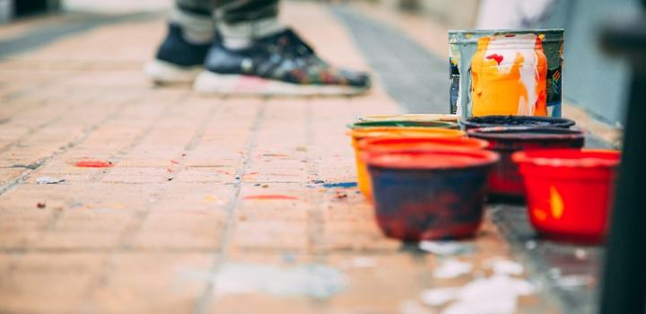 Tarros de pintura en la vereda y de fondo unos pies frente a un muro.