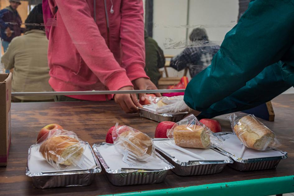 Manos entregando y recibiendo viandas con alimentos.