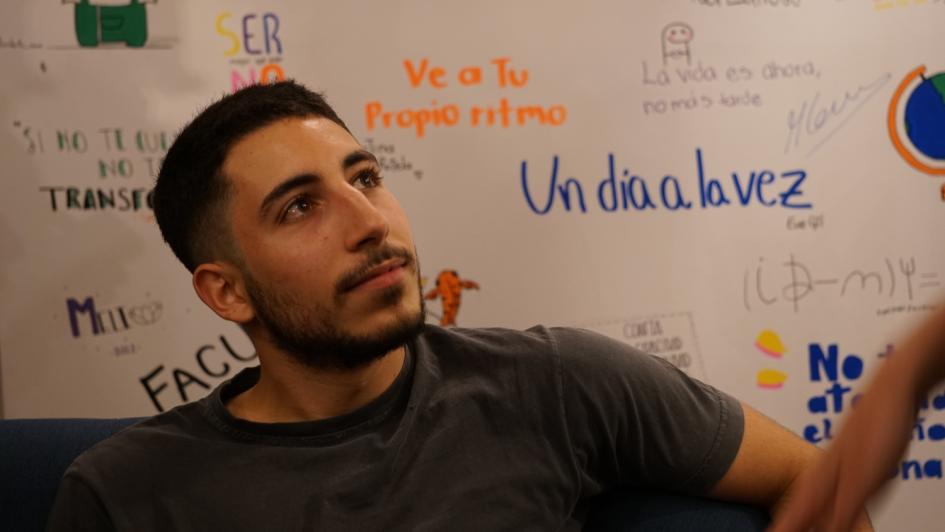 Estudiante residente en la CIU Hombre joven estudiante en silllón, mira hacia arriba, al fondo pared con frases motivacionales