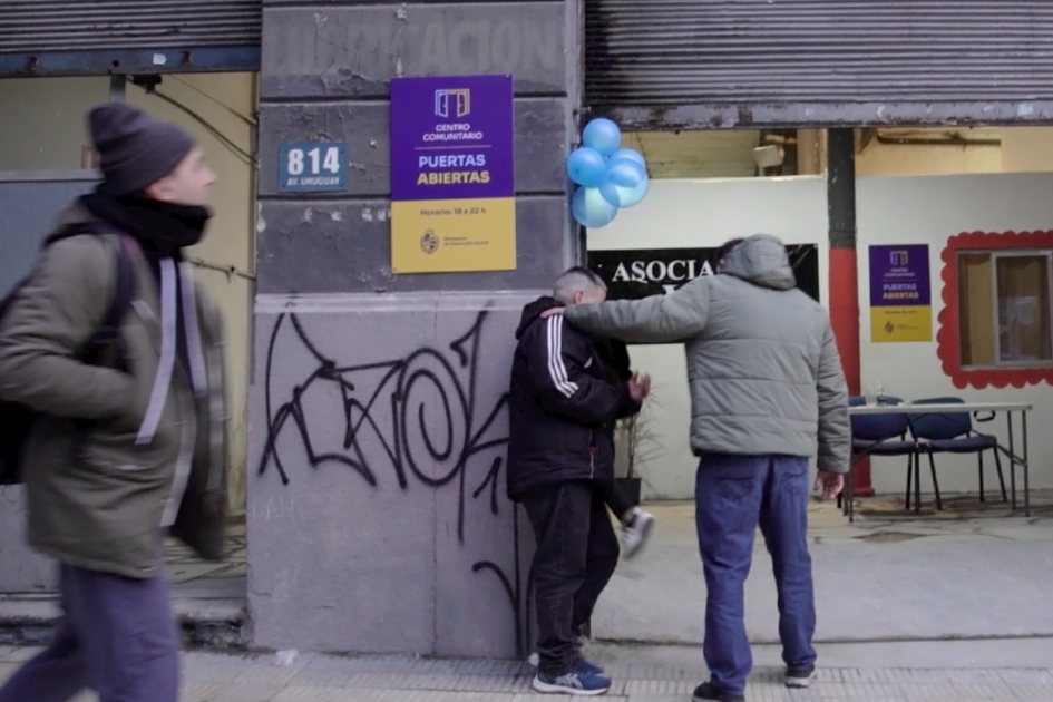 Entrada al centro "Puertas Abiertas" en Ciudad Vieja. Dos hombres ingresan al centro, otro transeúnte pasa caminando junto a ellos.