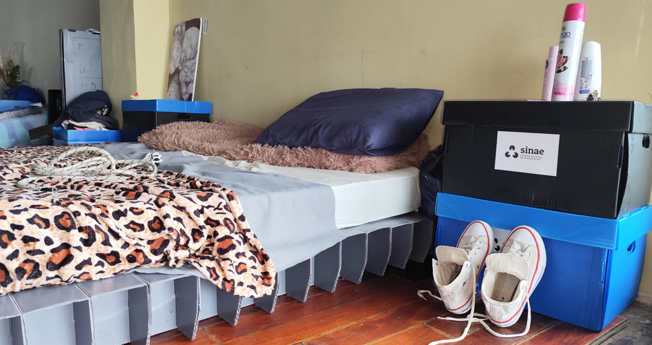 Cama con cajas dispuestas como mesas de noche en un Centro de Evacuados