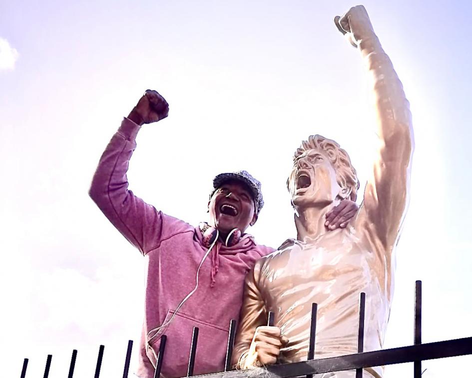 Hombre en estadio de Peñarol junto a la estatua de Fernando Morena imita el gesto de brazo en alto.