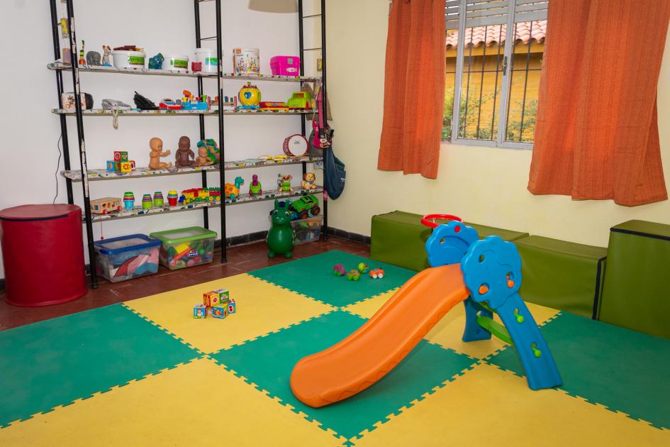 Salón de juegos y recreación de la Casa Comunitaria de Cuidado "María Abella" para la primera infancia Salón de juegos con tobogán, piso de goma eva y juguetes para niños menores de 2 años