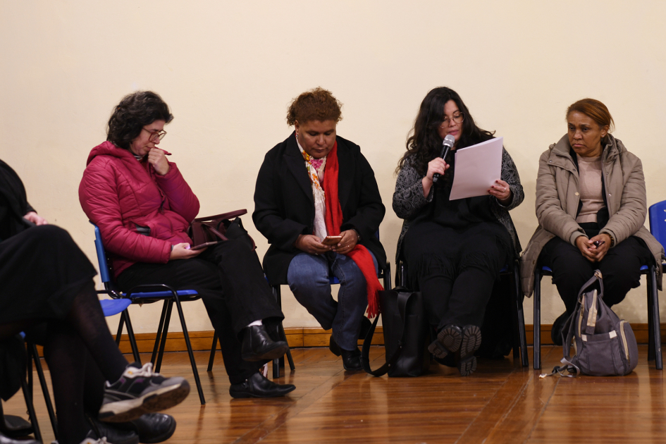 Técnicas del Área de Diversidad del ministerio junto a representantes de organismos públicos. Varias mujeres sentadas juntas. Una de ella con micrófono en mano lee proclama.