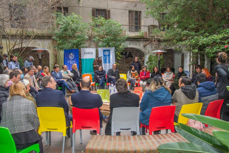 Foto de espalda de personas sentadas en ronda en sillas de distintos colores