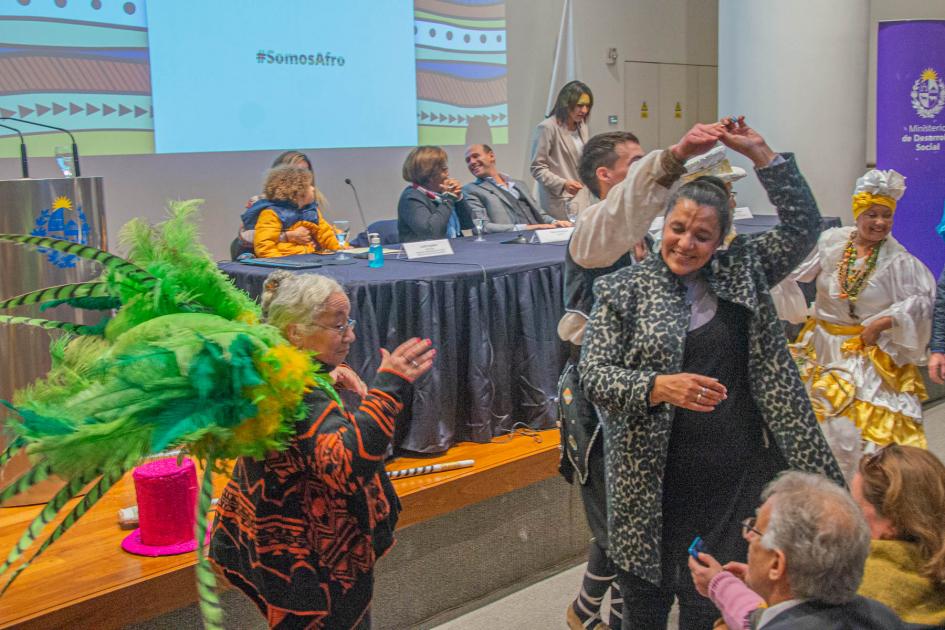 Comparsa C1080 cierra jornada de presentación del Mes de la Afrodescendencia Activistas y público con plumas y ropa de comparsa bailan al ritmo de los tambores