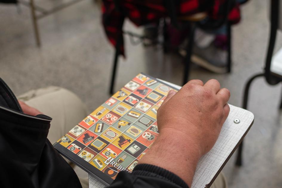 Participante de Programa Mides en su primer día de clase Cuaderno sobre apoya brazos, encima mano de estudiante