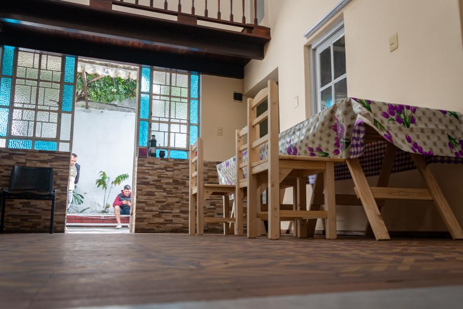 Interior de la casa hogar de medio camino, cocina comedor, mesas y bancos de madera color natural.