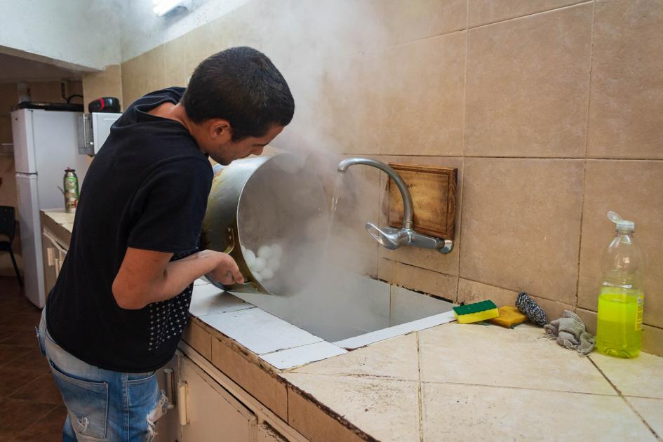 Hombre joven en la cocina de la Posada, tirando contenido de agua calente de una olla