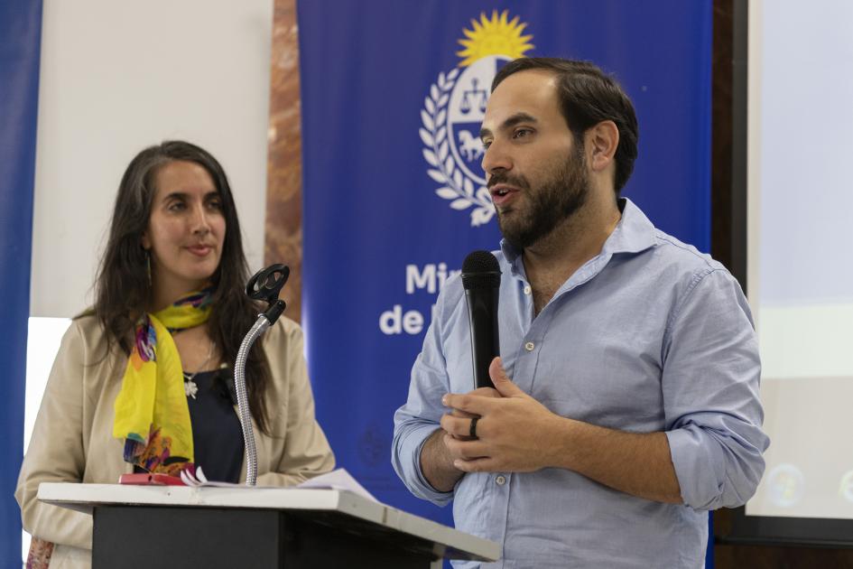 Ministro Civila junto a Marianela Larzábal durante la presentación del evento. Ministro Civila, de pie, con camisa arremangada, sostiene micrófono. Al lado Marianela Lárzabal.