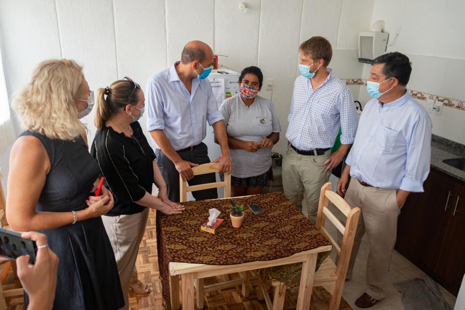 Interior de vivienda autoridades hablando con usuaria alrededor de una mesa