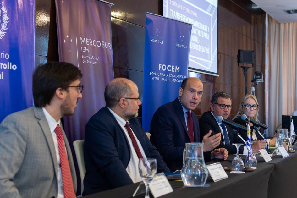 Los 5 integrantes de la mesa de oratoria atentos al discurso del ministro Lema. Al fondo banners.