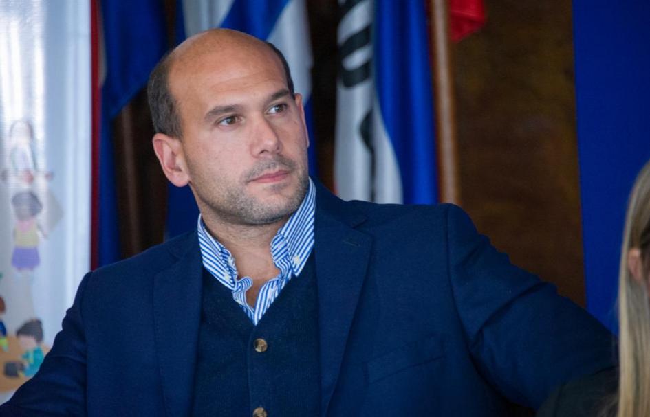 Ministro Lema en la presentación del Programa Acción Familiar de UCC - Foto Presidencia Ministro Lema sentado frente a los pabellones patrios observa el video de Acción Familiari