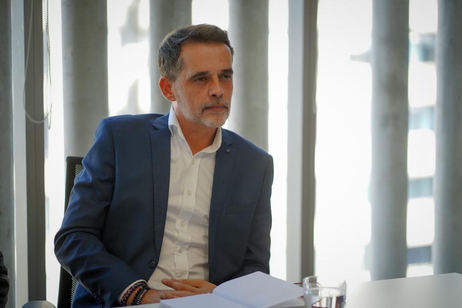 Subsecretario Federico Graña. Graña sentado a la mesa de reuniones, mira atento a interlocutora. De fondo ventanal con cortinas..