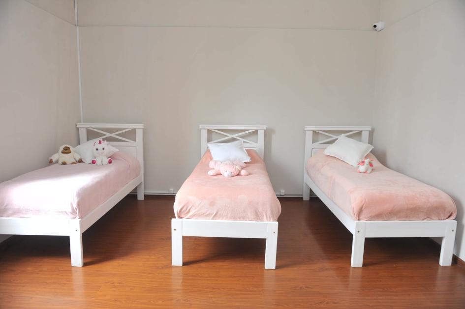 Otro de los dormitorios. Tres camas blancas con mantas rosadas y peluches encima.