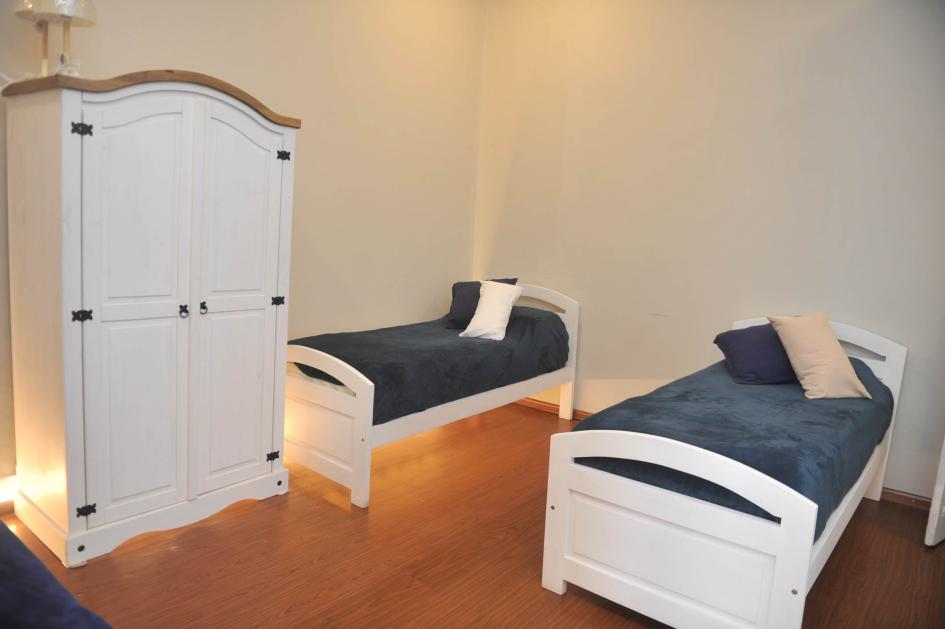Ropero blanco con herrajes y dos camas blancas con frazadas azules en uno de los dormitorios.