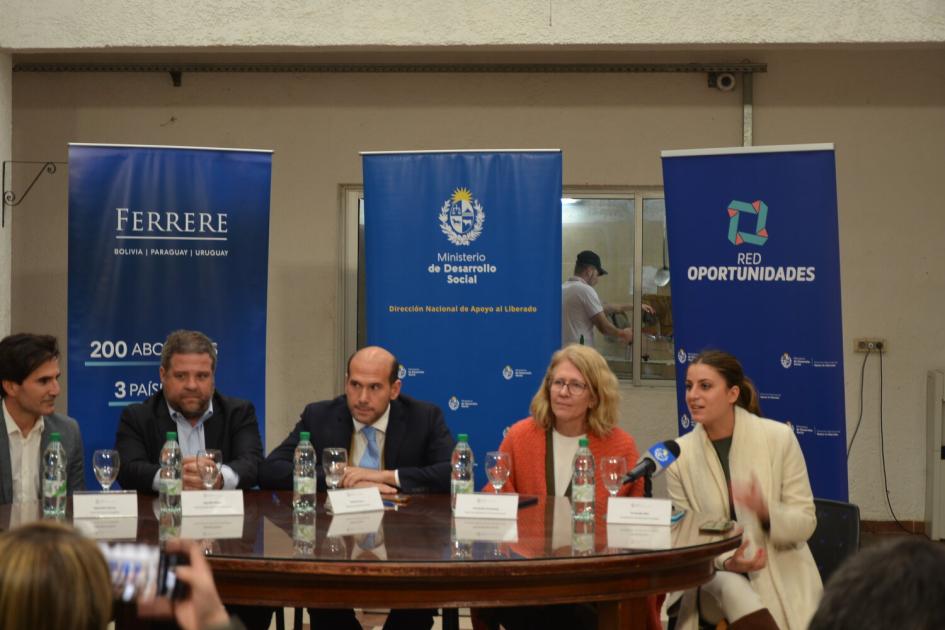 Tres hombres y 2 mujeres sentados entorno a la mesa de oratoria, detrás 3 banners de los organismos.