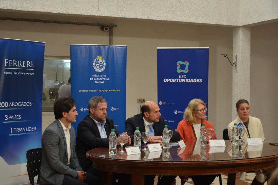 . Tres hombres y 2 mujeres sentados entorno a la mesa de oratoria, detrás 3 banners de los organismos.