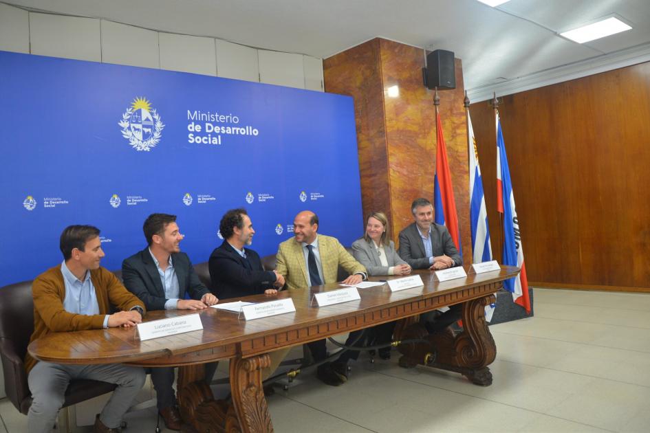 Mesa con pabellones patrios y banner de fondo. Lema junto a autoridades del Mides y de Ingener