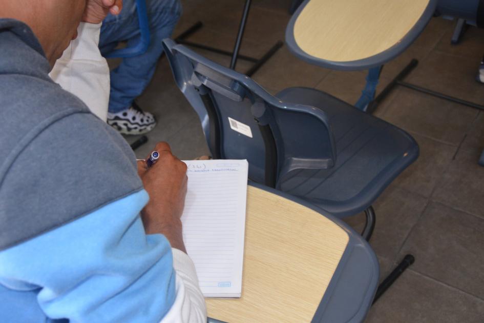 Participante del curso Operador en Logística dictado en DINALI por Adra e Inefop Estudiante en actitud pensativa escribe en cuaderno mientras se apoya en codo derecho
