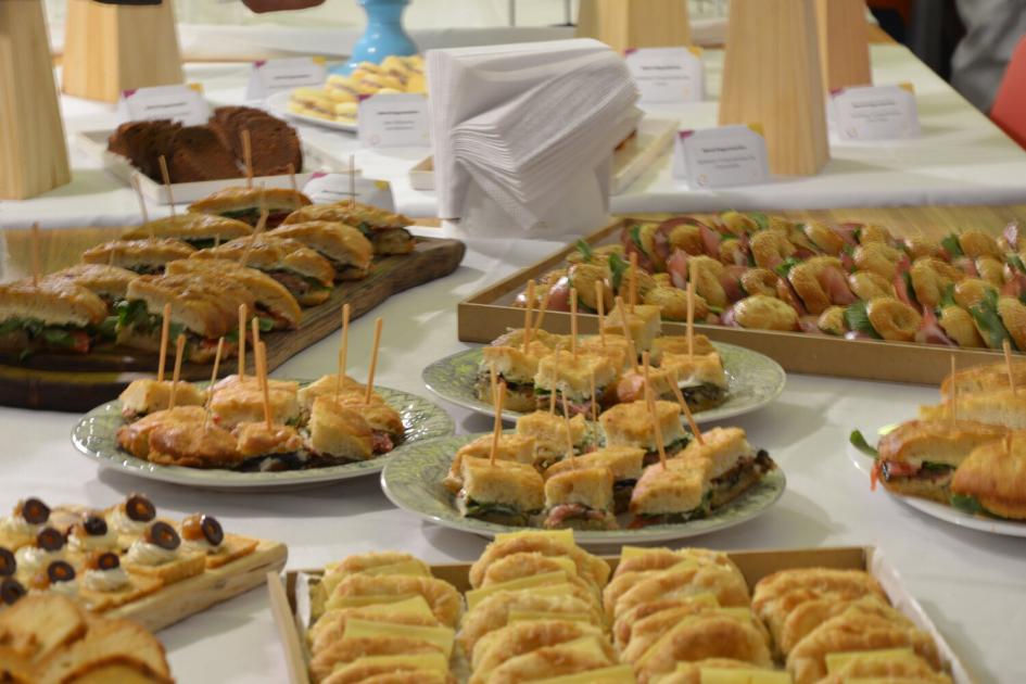 Productos manufacturados por participantes sin hogar que se capacitan en gastronomía. Mesa con bandejas y platos que contienen masas, bizcochos, bocatas, saladitos.