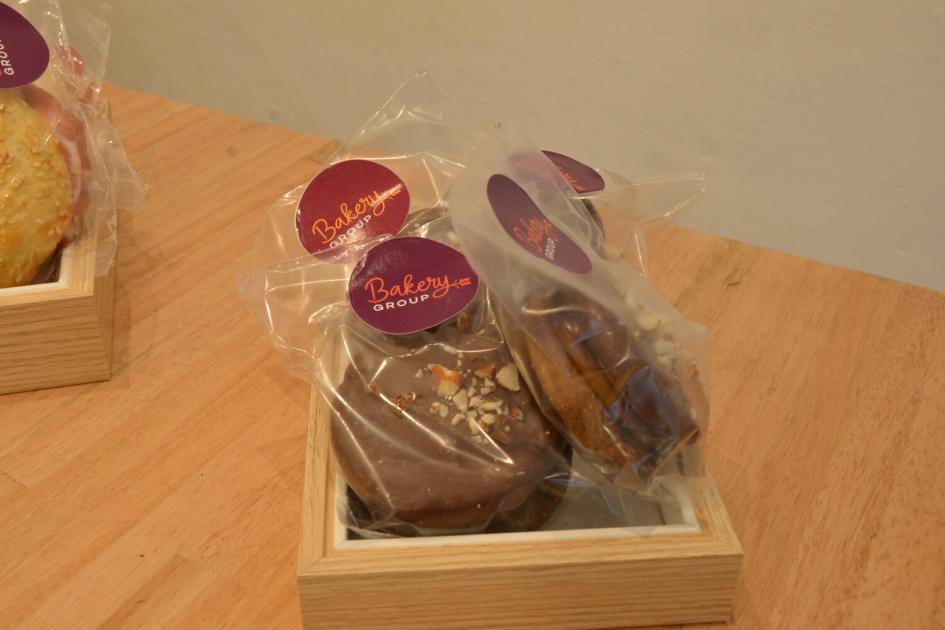 Productos elaborados por usuarios de refugios en curso de Gastronomía. Alfajores de chocolate en envoltorios individuales con etiqueta circular roja en cajón de madera.