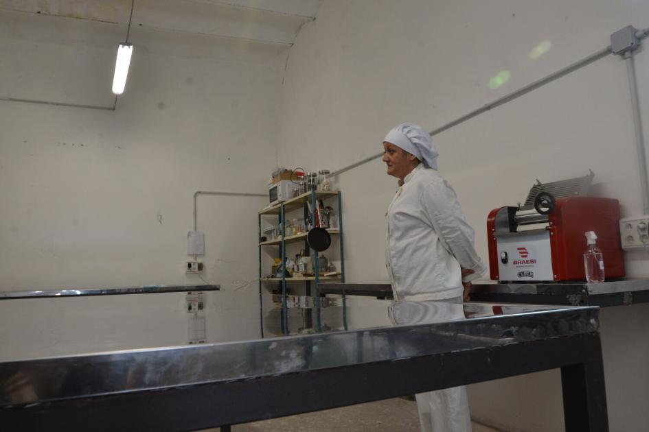 Participante del taller en la cocina de la cooperativa. Mujer vestida de chef en la cocina de la cooperativa, mesada amplia de acero , electrodomésticos.