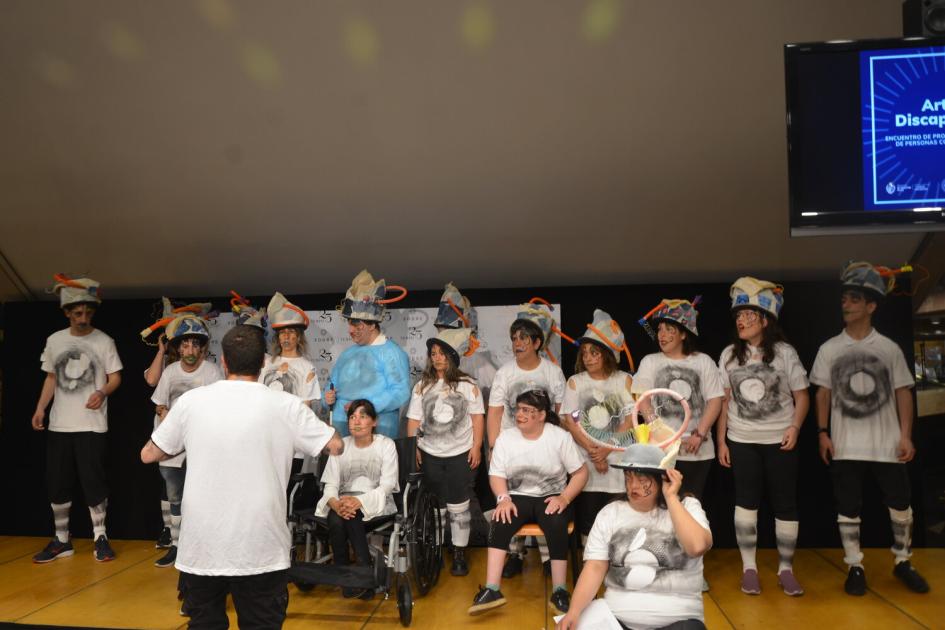 Murga integrada por jóvenes con discapacidad, algunos de pie, otros en silla de ruedas, en escenario