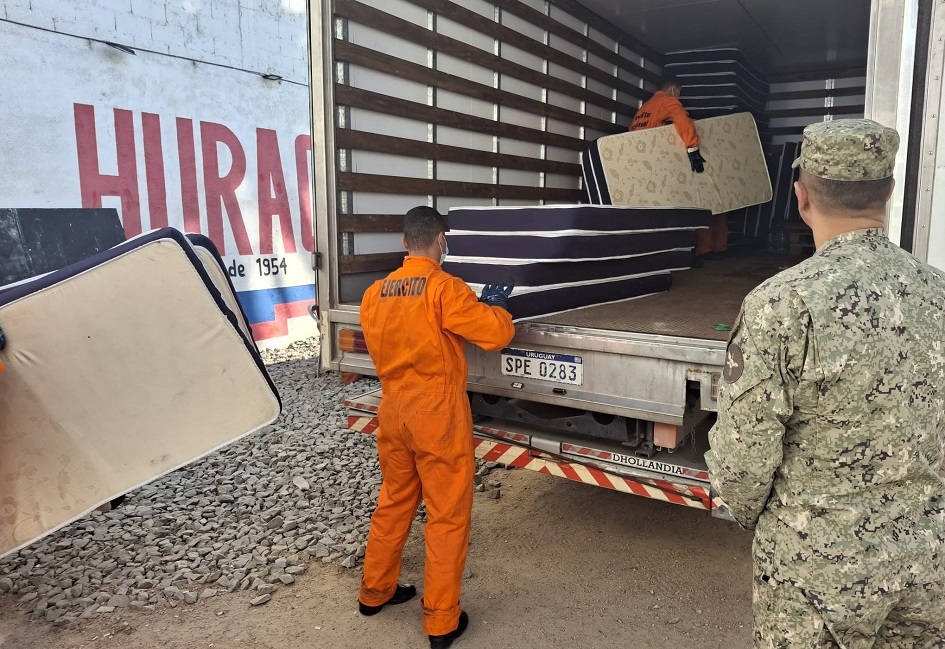 Dos personas de uniforme suben colchones a un camión Personal del ejército cargando colchones en la caja de un camión