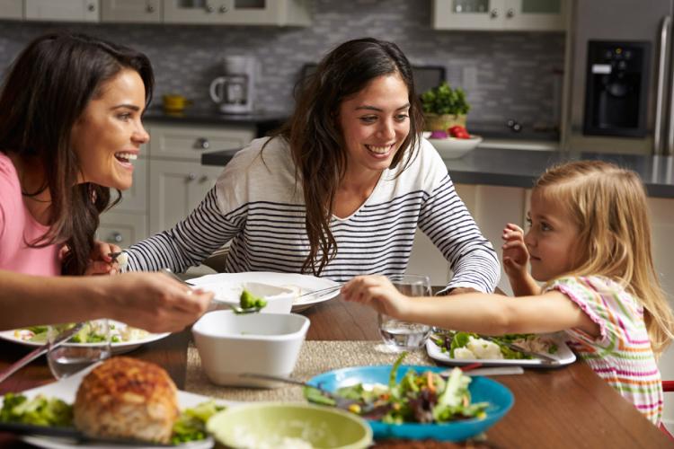 Dos mujeres y una niña comiendo en torno de una mesa