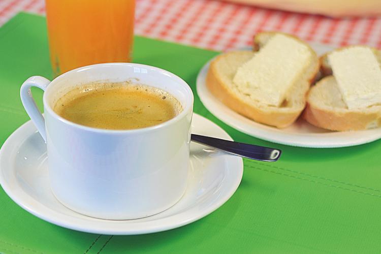 Taza de café con leche, un vaso de jugo de naranja y dos tostada con queso, todo sobre un mantel verde